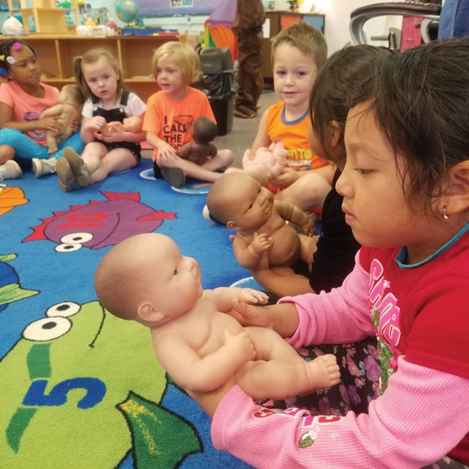 Young Kids Gathered Around on Rug and Holding Baby Dolls