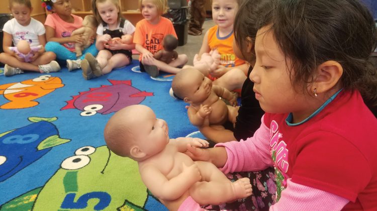 Young Kids Gathered Around on Rug and Holding Baby Dolls