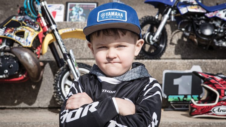 Young Boy with Arms Folded Standing In Front of Dirt Bikes