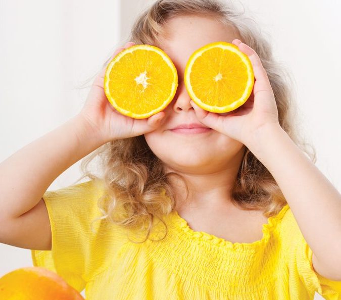 Little Girl Holding Two Oranges up to Her Eyes