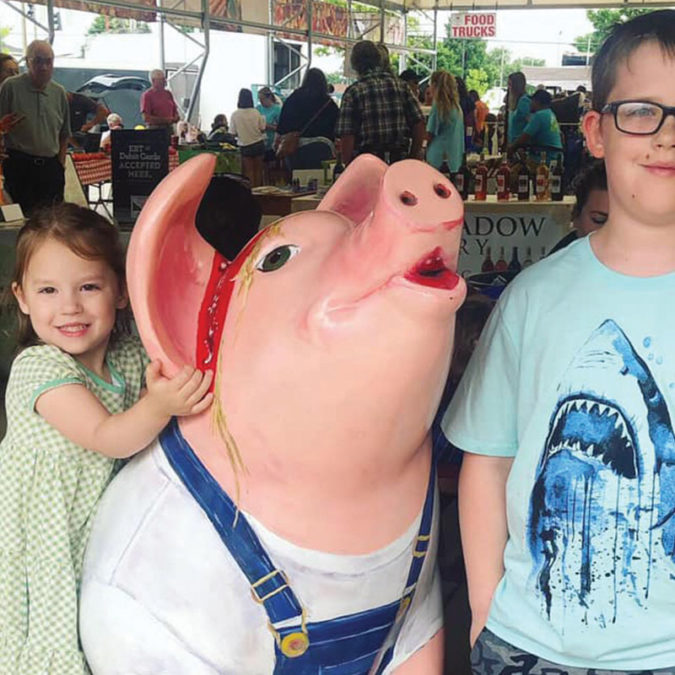 Kids pose next to a pig statue