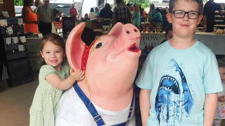 Kids pose next to a pig statue