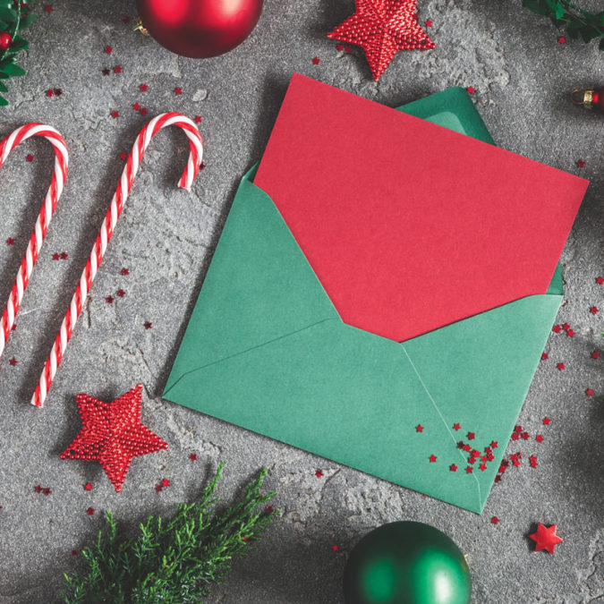 Overhead photo of red and green Christmas card in envelope, fake candy canes, presents and ornaments