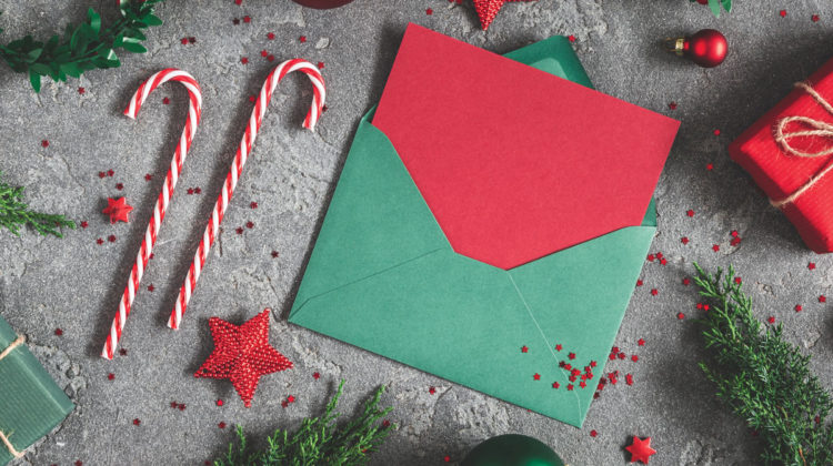 Overhead photo of red and green Christmas card in envelope, fake candy canes, presents and ornaments