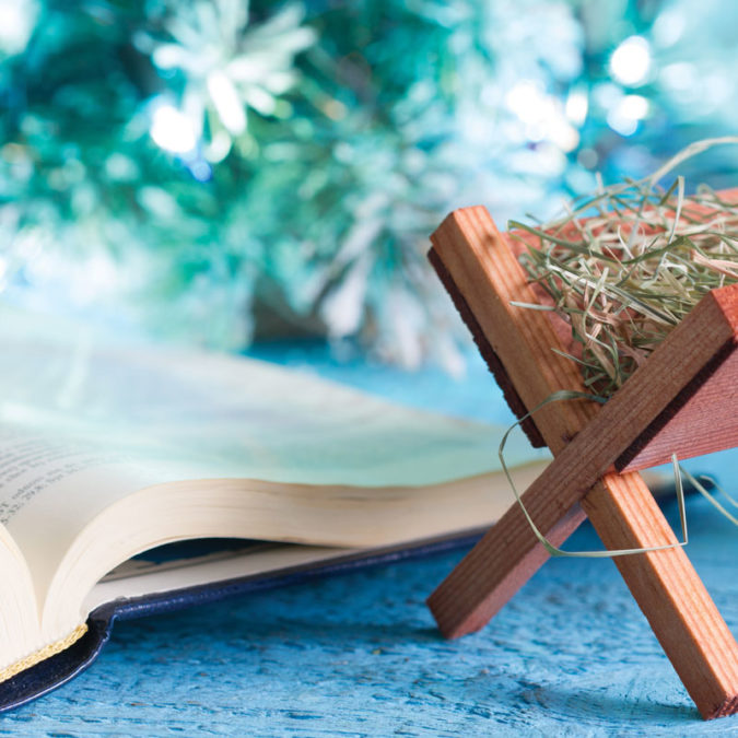 Tiny wooden manger beside Bible sitting on table