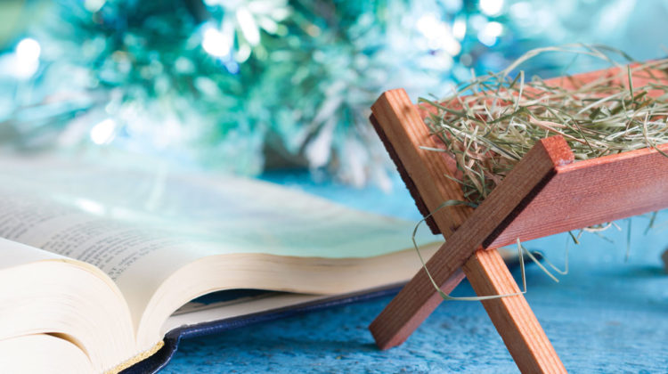 Tiny wooden manger beside Bible sitting on table