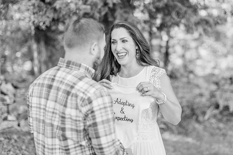 The Howards hold baby clothing that says "Adopting and Expecting"