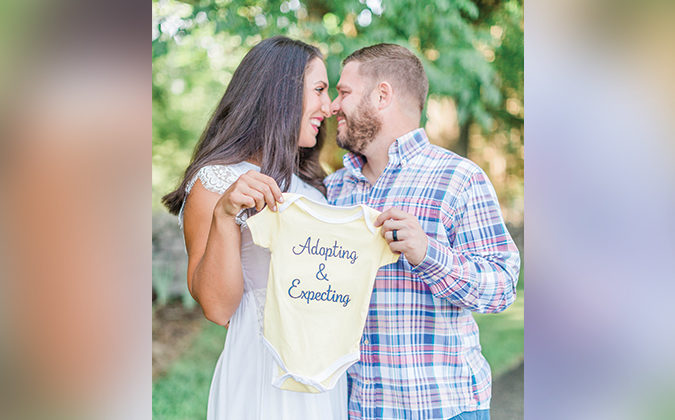 The Howards hold baby clothing that says "Adopting and Expecting"